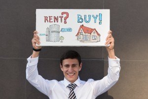 Man holding a sign that talks about renting versus buying a home